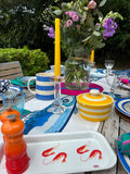 Outdoor setting with flowers, glasses, and a colorful tray on a wooden table.