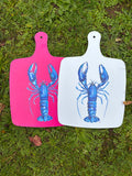 Two cutting boards with blue lobster designs on a grassy background