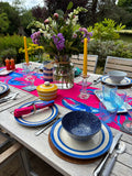 Outdoor table setting with colorful  Lobster runner, plates, and flowers on a wooden deck.